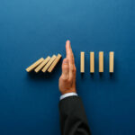hand stopping dominos from falling, represent a crisis being prevents or stopped