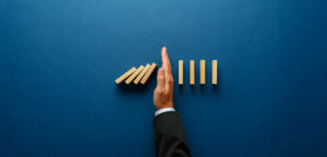 hand stopping dominos from falling, represent a crisis being prevents or stopped