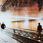 Two people riding a moving sidewalk into a bright white void to represent transformation