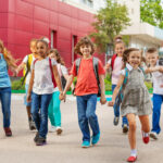 Happy kids with rucksacks walking leaving school