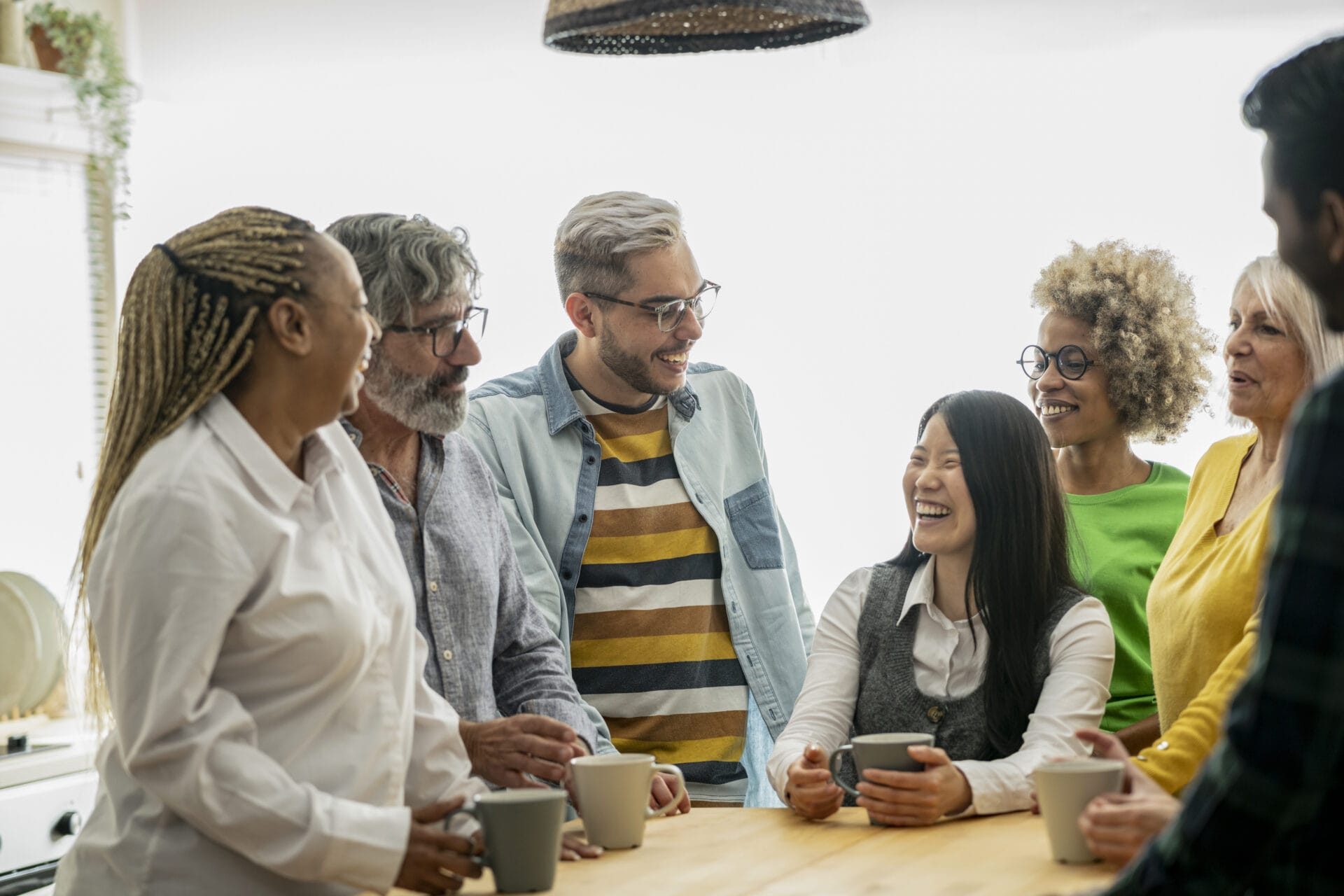 A vibrant, multigenerational team shares laughter and conversation over coffee in a naturally lit, relaxed office setting. Workplace safety culture, safety leadership, employee engagement in safety, accountability in workplace safety